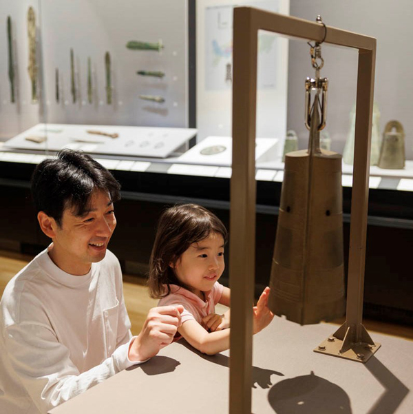 銅鐸（レプリカ）を鳴らす親子の様子